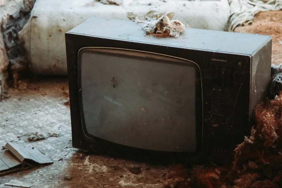 A neglected CRT television amidst debris in a decaying interior, evoking nostalgia.