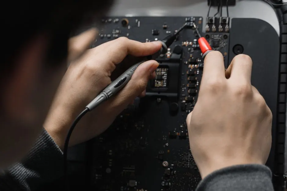 Close-up of hands repairing a circuit board using a soldering iron, emphasizing technical skill.