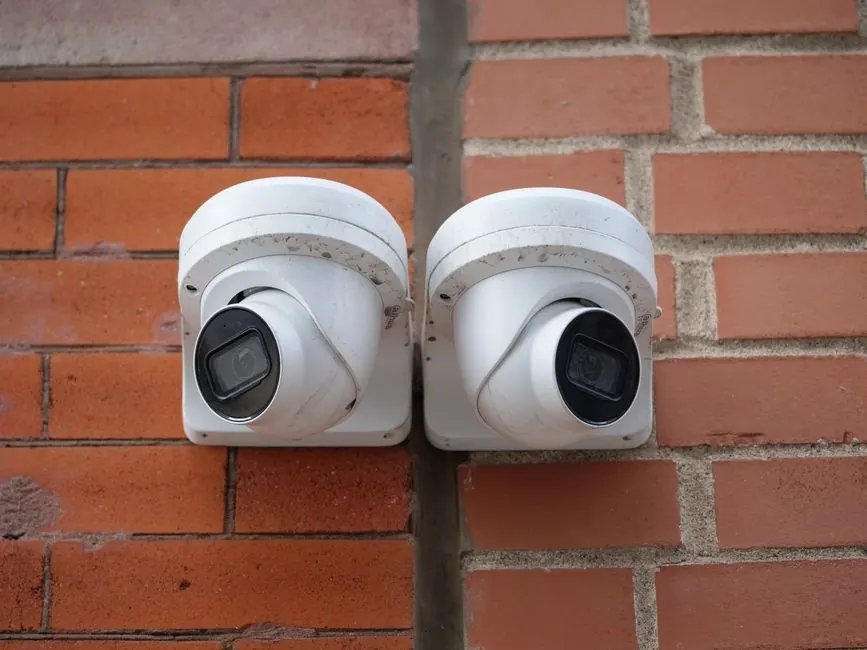 Two white dome security cameras mounted on a brick wall for urban surveillance.
